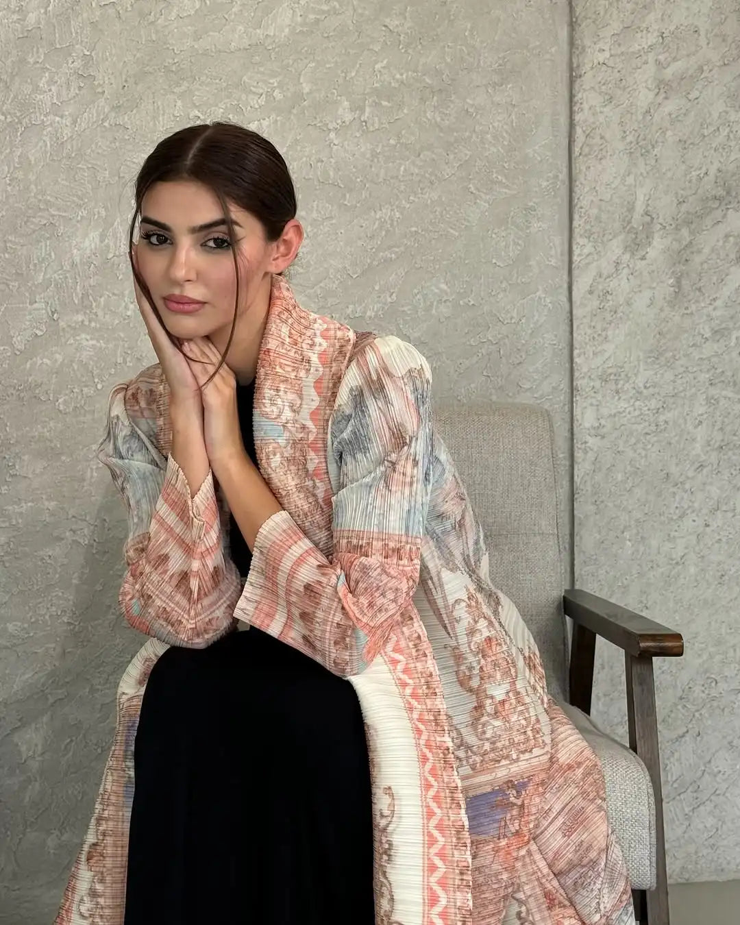 Eine Frau trägt eine fließende, plissierte Abaya-Cardigan in rosa und beige vor grauem Hintergrund.