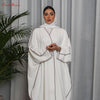 Una mujer vistiendo una abaya blanca oversize con ribetes marrones, vestido modesto de largo completo.