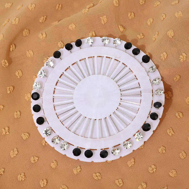 Pince ou broche de hijab en cristal strass rond blanc avec accents noirs, présentée sur un tissu beige.