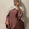 Eine Frau in einem maugen, fließenden, bodenlangen Abaya mit weiten Ärmeln und weißem Hijab, posiert für ein Foto.