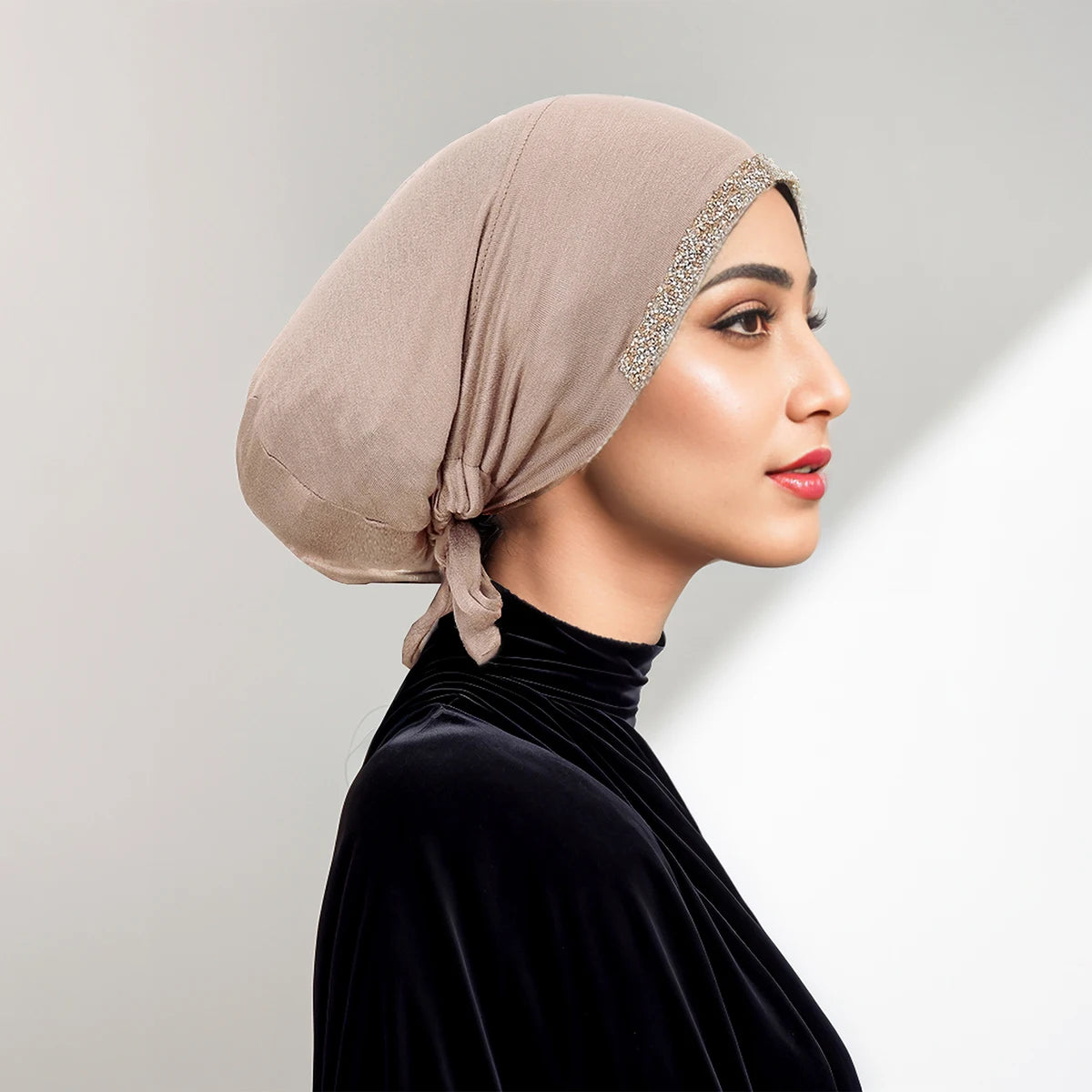Eine Frau trägt einen beige drapierten Hijab mit Strassbesatz und einem schwarzen Samt-Oberteil.