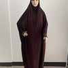 Un mannequin portant une caftan abaya ample bordeaux foncé avec un hijab noir et des poignets à motifs.