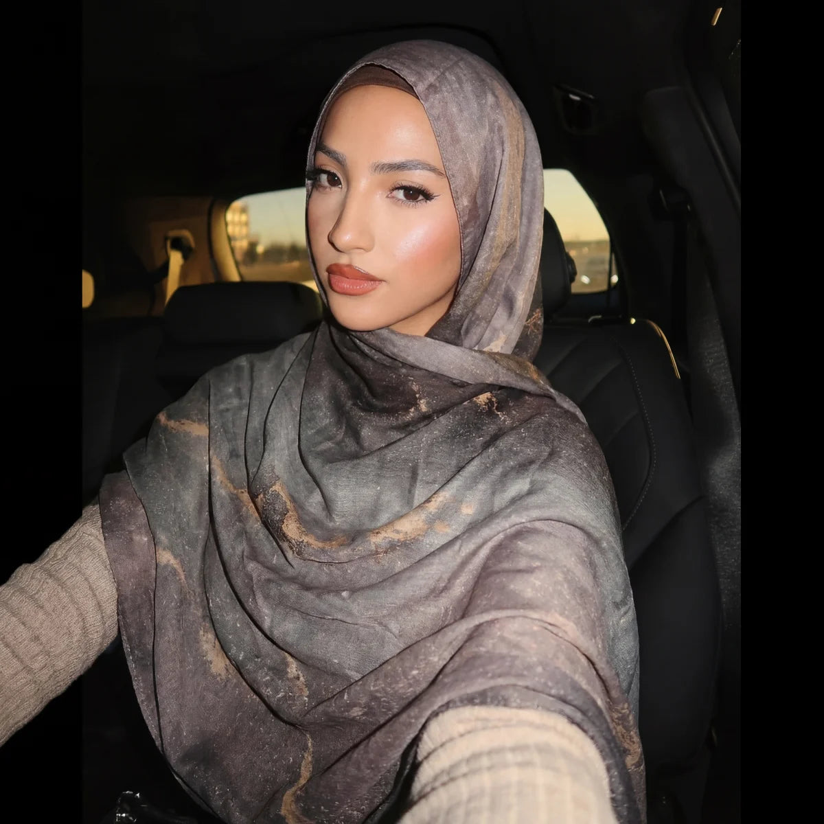 Eine Frau mit einem grauen Aquarellmuster-Schal-Hijab sitzt im Auto.