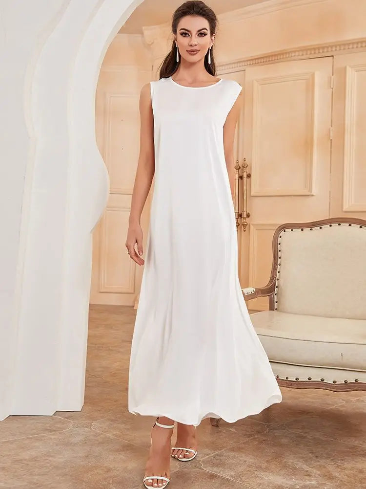 A woman models a white flowing modest abaya dress in a light beige room.