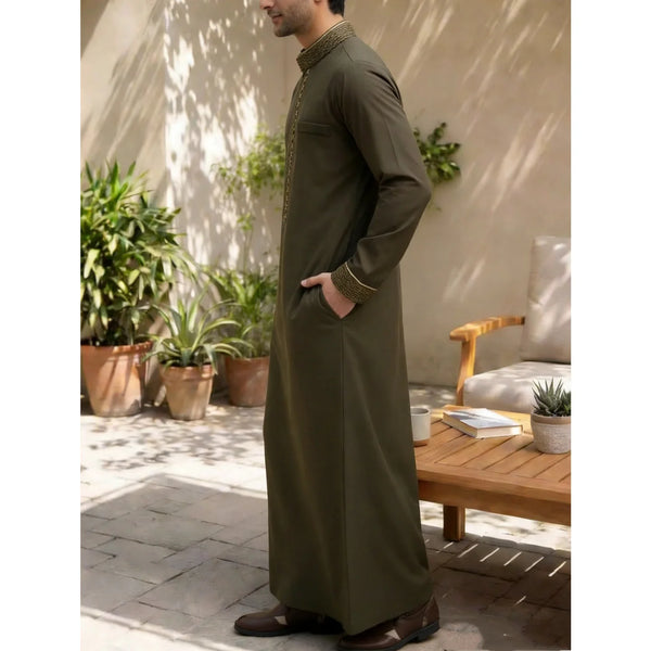 A man wearing a dark olive green traditional Islamic men's jubba thobe standing outdoors.