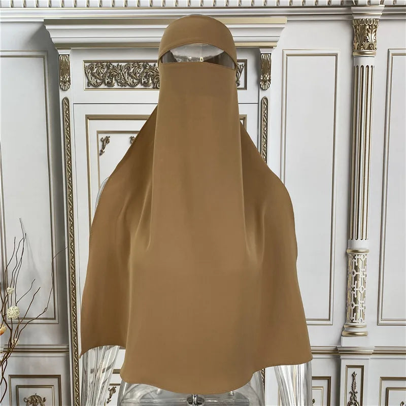 Beige elegante Maxi-Abaya über einem Aufsteller vor aufwendigem weiß-goldenem architektonischem Hintergrund.