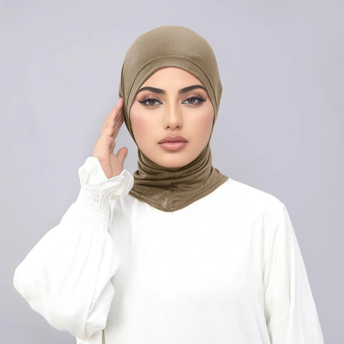 Eine Frau trägt einen beigen Instant-Turban-Hijab, eine Unterkappe und ein weißes Oberteil.