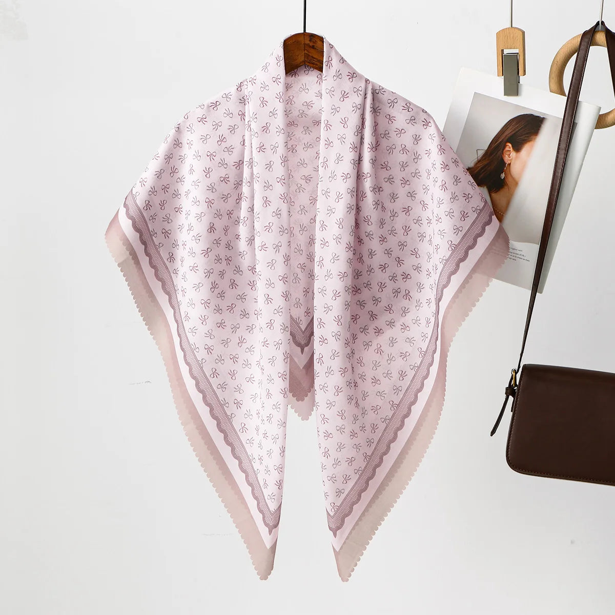 Helles rosa Blumen-Quadrat-Hijab-Schal auf Holzständer vor weißem Hintergrund.