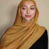 Eine Frau trägt einen goldbraunen Farbverlauf-Rayon-Modalfächer als Hijab über Kopf und Schultern.