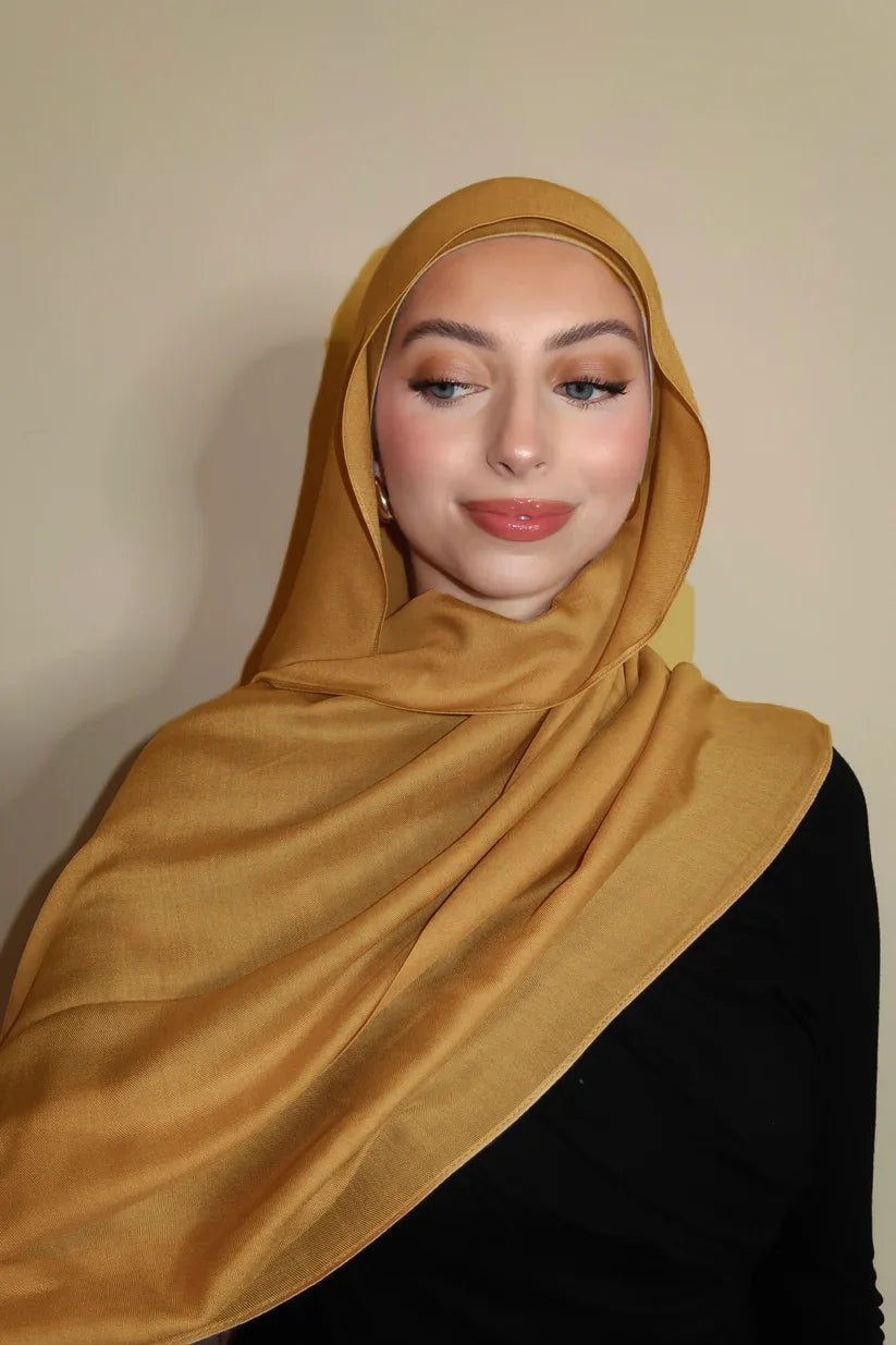 Eine Frau trägt einen goldbraunen Farbverlauf-Rayon-Modalfächer als Hijab über Kopf und Schultern.