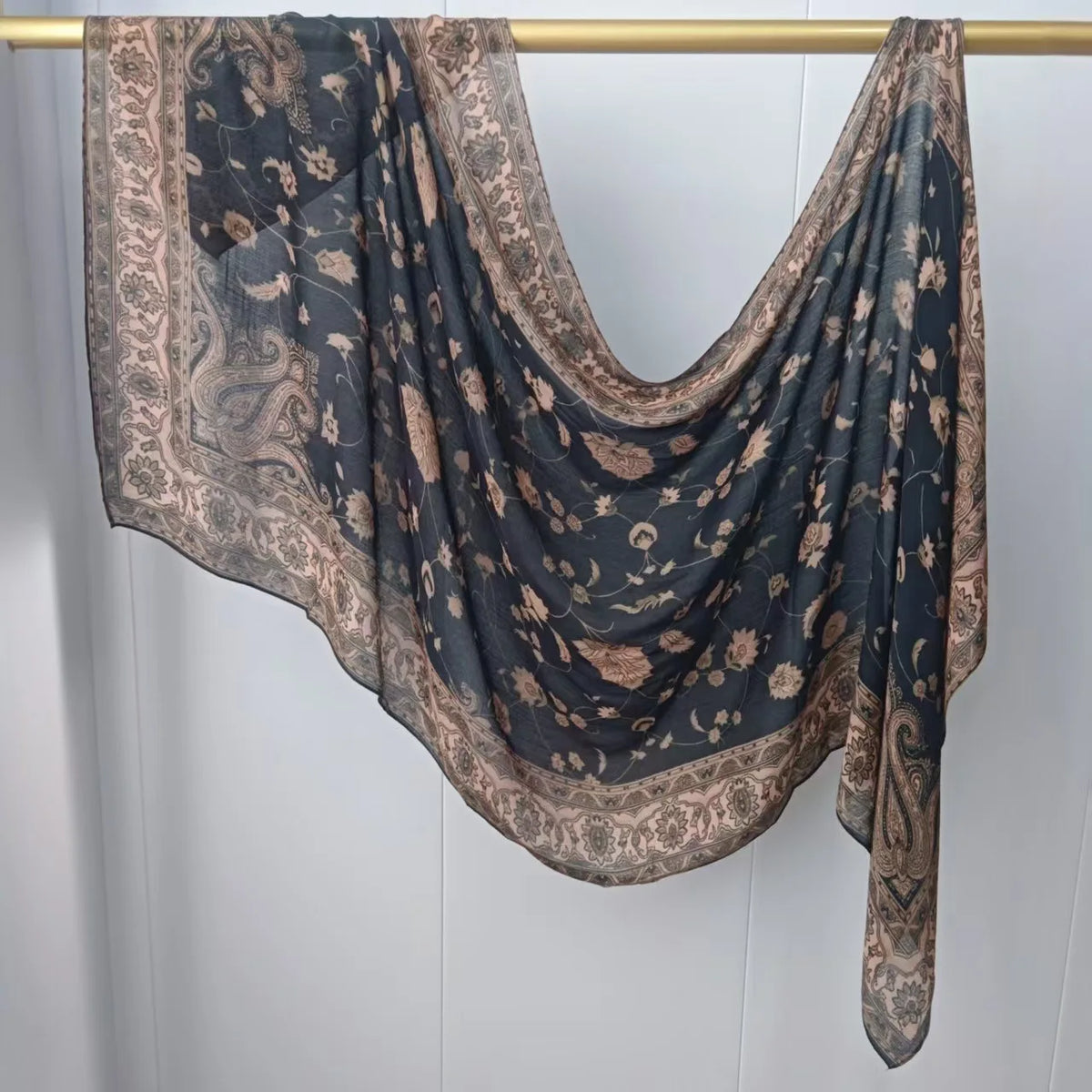 Dunkel gemusterter Hijab-Schal, drapiert über einem Holzbügel.
