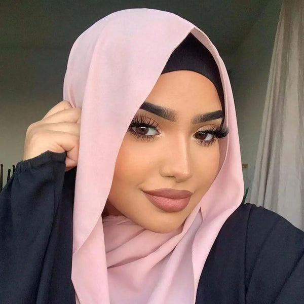 A woman wearing a light pink chiffon hijab scarf with black undercap and dark clothing.