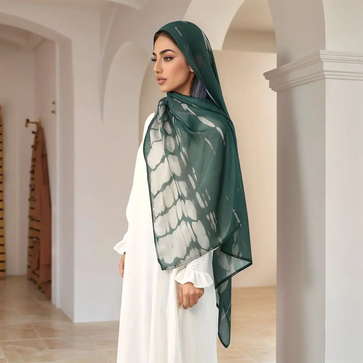 Eine Frau trägt einen durchscheinenden, aquarellartigen digitalen Hijab-Schal in Grüntönen und Weiß in einem hellen Innenraum