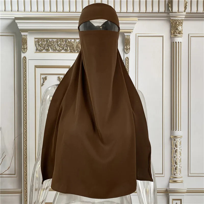 Braune elegante Maxi-Abaya auf einem Mannequin vor weißer verzierten Wandvertäfelungen.