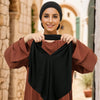 Eine Frau modelliert einen schwarzen Instant-Hijab-Schal aus weichem Modaljersey in einem terrakottabraunen Oberteil.