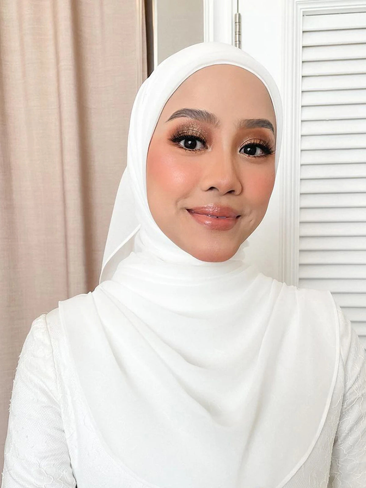 A woman wearing a white hijab and matching inner scarf set looking at the camera.