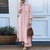 Una mujer vistiendo un conjunto de abaya rosa largo y una hijab blanca, de pie frente a una puerta blanca.