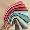 Eine Hand hält einen Stapel rosa, blau und grauen Satin-Crinkle-Hijab-Schals.