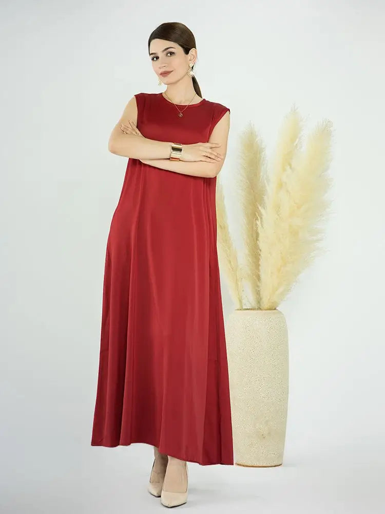 A woman wearing a flowing, modest maroon abaya dress stands next to a tall vase of dried beige pampas grass.