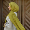 Une femme portant un foulard modal vert lime et un haut blanc devant des portes en bois.