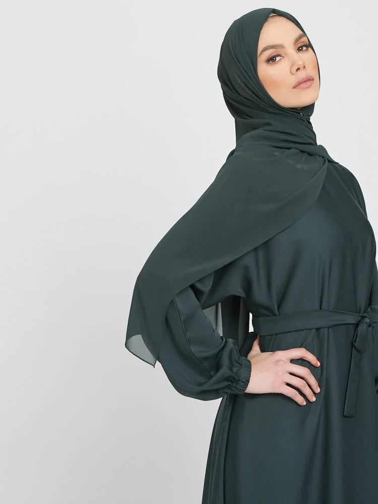 Eine Frau trägt eine dunkeltürkise marokkanische Kaftan-Abaya mit einem drapierten Kopftuch.