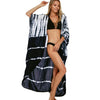 Eine Frau in einem schwarzen Bikini und einem locker fallenden, tie-dye gemusterten Kimono-Überwurfkleid.