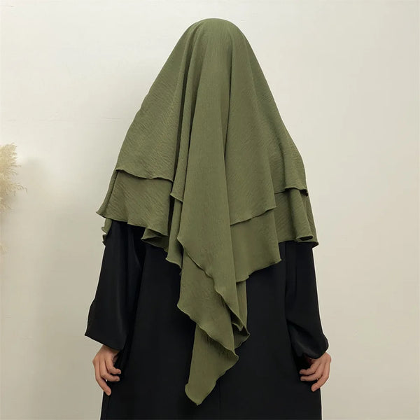 A woman wearing a olive green two-layer everyday hijab scarf over a black garment.