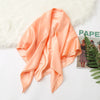 A flowing peach colored silk satin hijab scarf draped over a white fluffy surface.