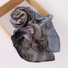 Un foulard voile imprimé drapé, en nuances de gris et de violet, est exposé sur un cadre en bois.