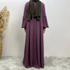 Eine Frau trägt ein elegantes langes lila islamisches Kleid und einen dunkelgrünen Hijab.