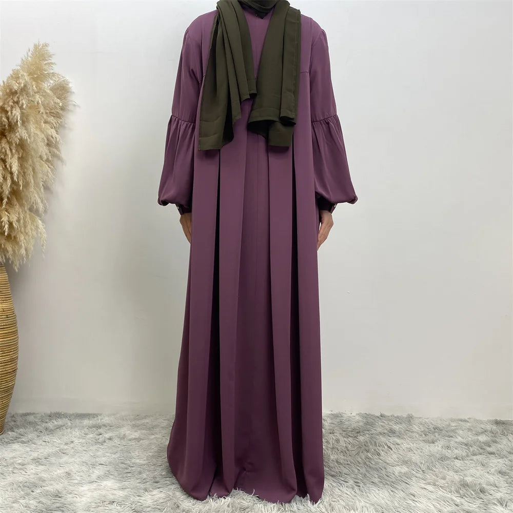 Eine Frau trägt ein elegantes langes lila islamisches Kleid und einen dunkelgrünen Hijab.