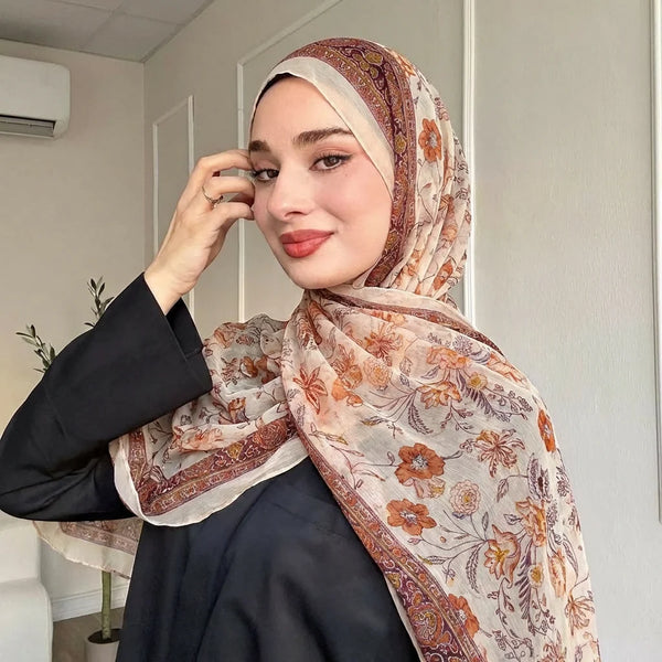 A woman wearing a floral printed voile shawl hijab with a dark top, posing for a portrait.