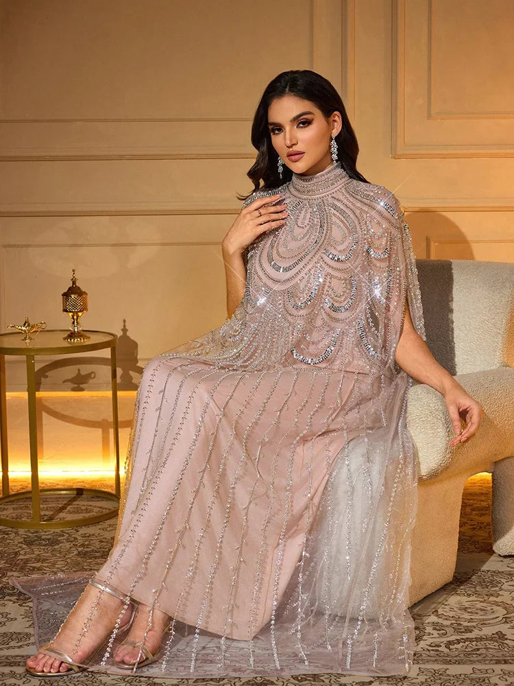 Una mujer modela una elegante bata con alas de murciélago y delicados bordados de plata en color rosa polvoriento.
