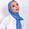 Una mujer vistiendo un pañuelo de hijab de algodón premium azul y una camisa blanca.