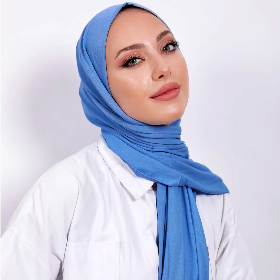 Una mujer vistiendo un pañuelo de hijab de algodón premium azul y una camisa blanca.