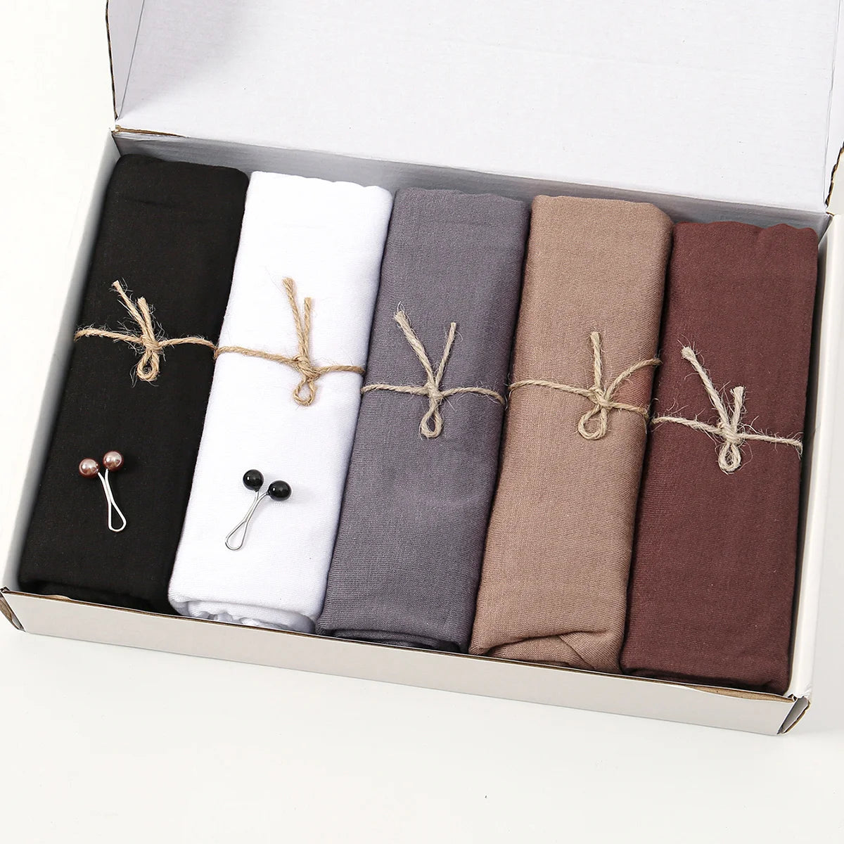 Eine Box mit einem Set von fünf Jersey-Hijab-Schals in Schwarz, Weiß, Grau, Beige und Braun.