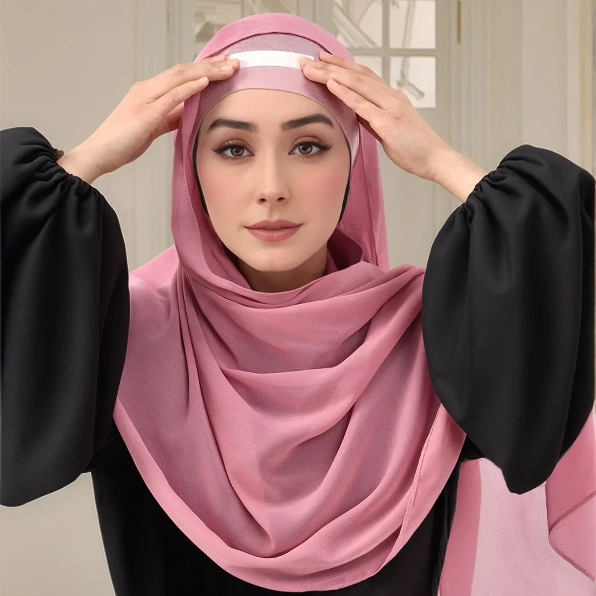 Una mujer con un hiyab rosa ajusta la tela con sus manos.