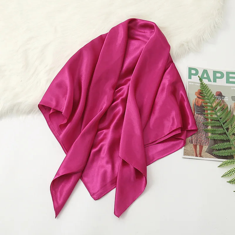 A vibrant magenta silk satin hijab scarf draped over a white faux fur rug.