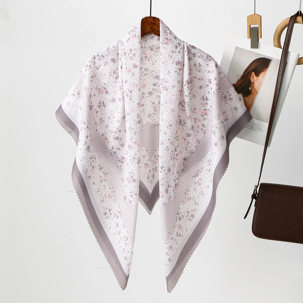Helles rosa Blumen-Quadrat-Hijab-Tuch auf einem Haken vor weißem Hintergrund.
