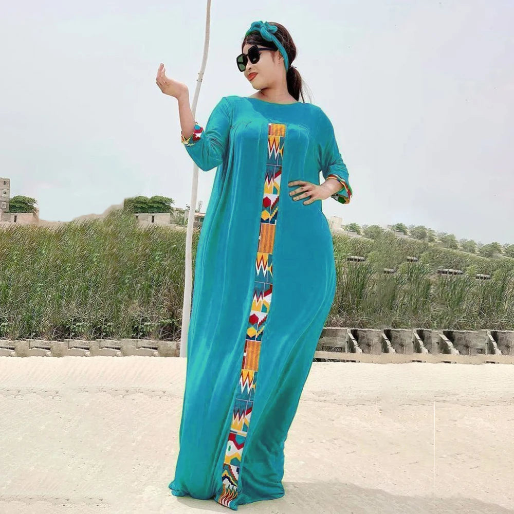 Eine Frau in einem türkisen Kaftan-Set mit farbenfroher Stickerei steht draußen vor einer trockenen Landschaft.