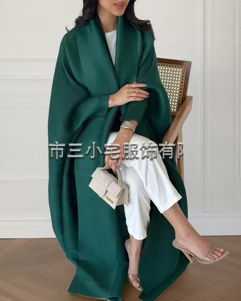 Una mujer vistiendo un cárdigan abaya plisado verde esmeralda oscuro sobre ropa blanca.