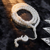 Tasbih de cuentas blanco con borlas de luna y estrella sobre una superficie oscura.