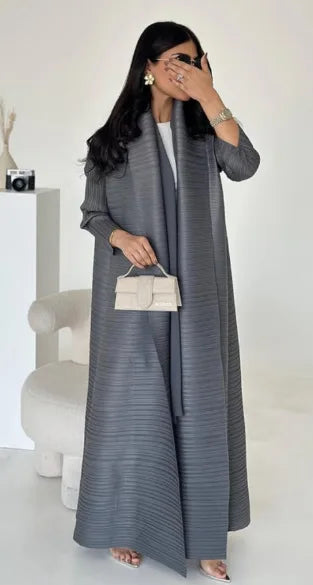 Une femme modélise une veste coupe-vent grise à plis, avec un haut blanc et des bijoux dorés.