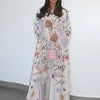 Una mujer modela un kaftan largo de color claro con estampado floral de flores rosas y azules.