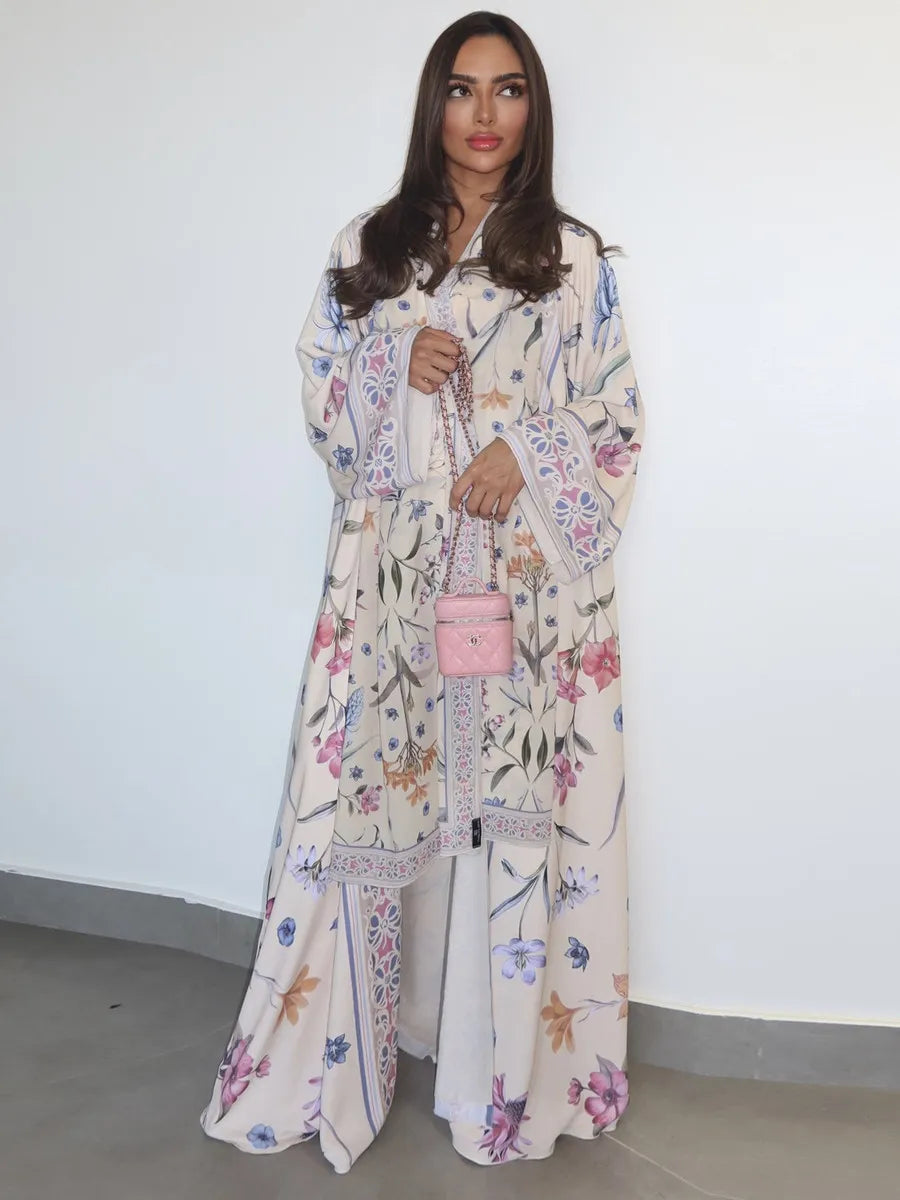 Una mujer modela un kaftan largo de color claro con estampado floral de flores rosas y azules.