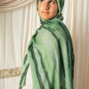 Eine Frau trägt einen grünen aquarelligen gestreiften Hijab-Schal vor hellem Hintergrund.