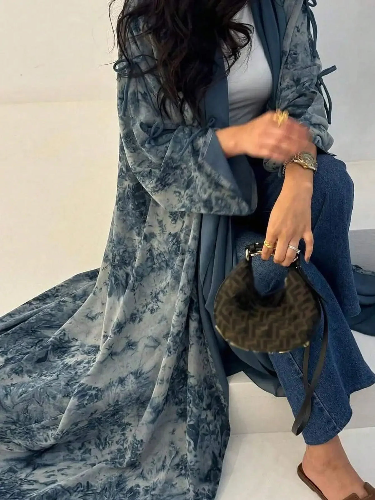 Eine Frau trägt ein fließendes blau-graues Tie-Dye-Abaya Kaftan über blauen Jeans.