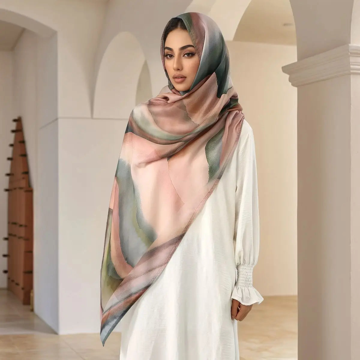 A woman wearing an elegant printed linen hijab scarf in shades of pink, green, and beige.