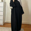 Une femme portant une élégante abaya noire ample et fluide avec un hijab gris et des accents argentés.