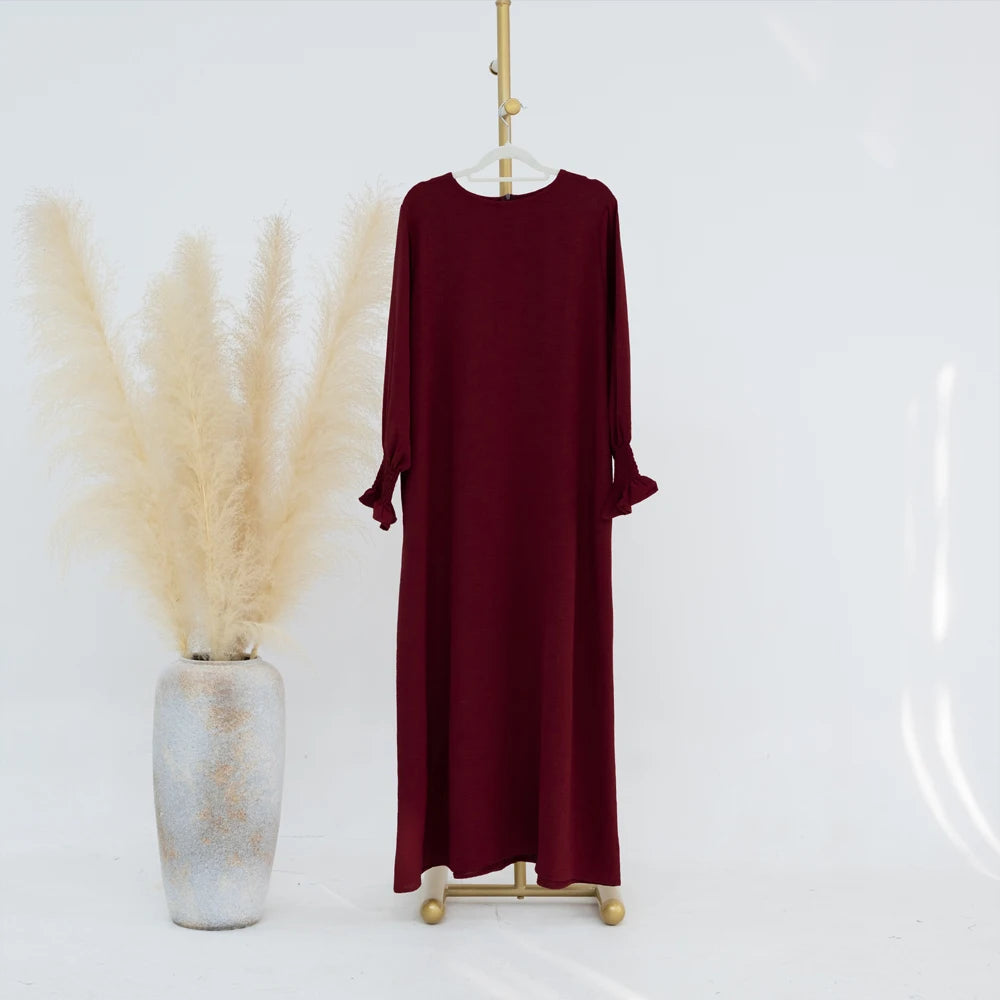 Vestido abaya holgado color granate colgado en una percha contra un fondo blanco.